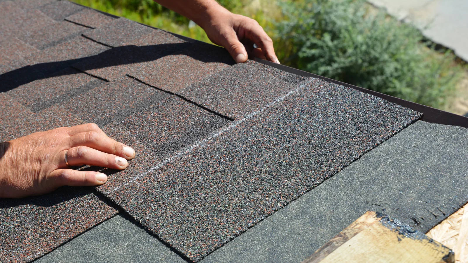 A roofer's hands laying asphalt shingle courses at a roof edge